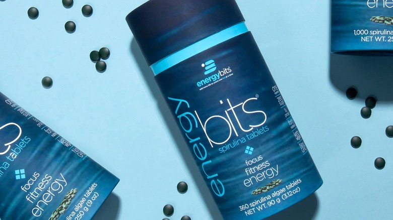 Container of ENERGYbits with pills around on blue background