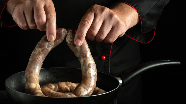 Hands placing two raw veal sausages into a frying pan