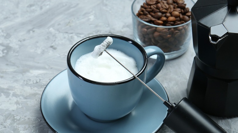 Milk frother lying against blue cup on saucer with frothed milk