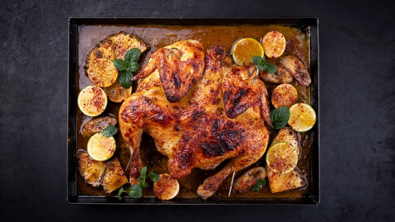 A spatchcocked chicken sits on a pan with BBQ sauce and fruit